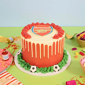 Football Cake by Crumbs & Doilies decorated with red and white drip, edible footballs, and a club crest topper.